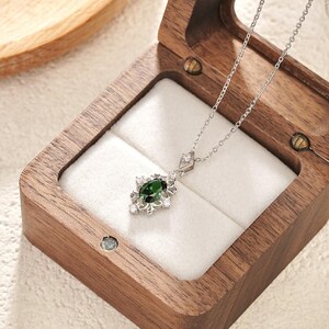 Pu&ograve; includere: Una collana d'argento con un pendente con una gemma ovale verde scuro circondata da piccole gemme bianche. La collana &egrave; esposta all'interno di un portagioie in legno con interno bianco.