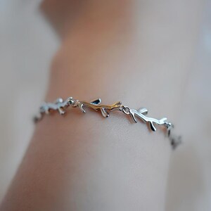 May include: A silver bracelet with a delicate design of intertwined branches. The bracelet is made of metal and has a polished finish.