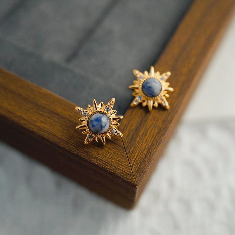 K&ouml;nnte beinhalten: Ein Paar goldene Sternburst-Ohrringe mit blauen und wei&szlig;en Steinen.