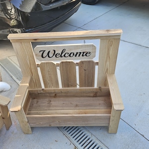 May include: A wooden chair with a planter box and a sign that reads "Welcome". The chair is made of light-colored wood and has a rustic design. The sign is rectangular and hangs from the top of the chair.