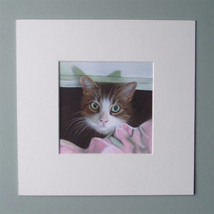 May include: A framed artwork featuring a cat with brown and white fur and green eyes. The cat is looking directly at the viewer. The artwork is framed with a white mat and a gray frame.