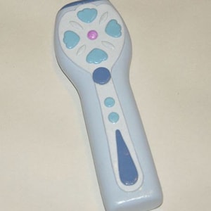 Może przedstawiać: Różdżka zabawka z plastiku w jasnoniebieskim kolorze z kwiatowym wzorem na górze. Kwiat ma pięć płatków i różowe centrum. Różdżka ma niebiesko-biały wzór na uchwycie.