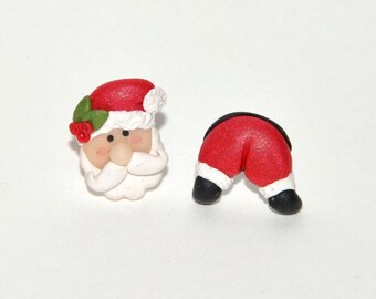 May include: Two Christmas-themed ornaments. One is a Santa Claus face with a red hat, white beard, and rosy cheeks. The other is Santa's red pants and black boots, trimmed with white. Festive holiday decor.