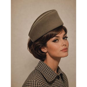 May include: A structured, olive-green felt pillbox hat with a smooth, rounded crown and a flat top. The hat features a clean, minimalist design with a solid color finish and a firm, upright silhouette that sits securely on the head.