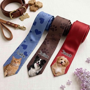 May include: Three neckties featuring pet portraits and names. The blue tie shows a ginger cat named Luke, the brown tie features a black and white dog named Julian with bone and paw prints, and the red tie displays a light brown dog named Jacob.