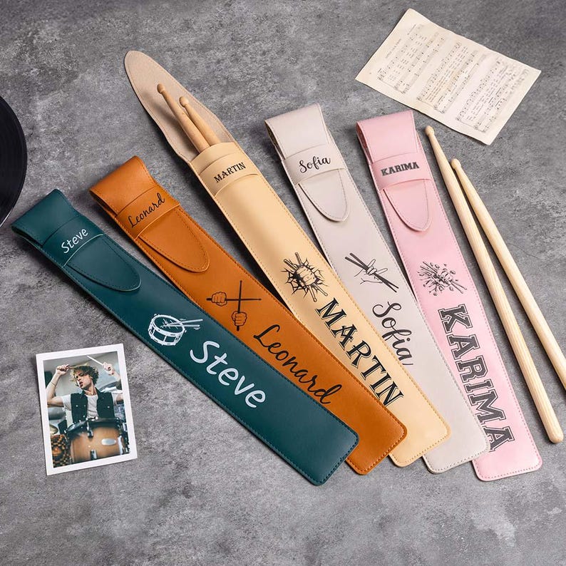 May include: Six personalized drumstick holders in various colors, including teal, brown, beige, and pink. Each holder has a different name and design, such as "Steve", "Leonard", "Martin", "Sofia", and "Karima".
