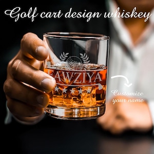 May include: A clear whiskey glass with ice cubes and amber liquid. The glass is etched with a golf ball design and the name "FAWZIYA". The text "Golf cart design whiskey" is above the glass.