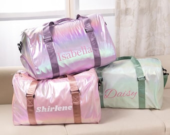 May include: Three iridescent pink and green duffel bags with pink lettering. The bags are personalized with the names "Isabella", "Shirlene", and "Daisy".