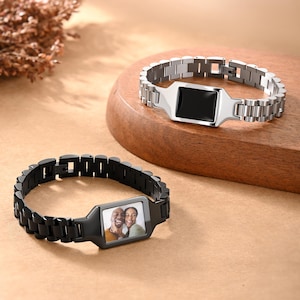 May include: Two metal bracelets. One is silver with a black rectangular center. The other is black with a rectangular center displaying a color photo of two people. Both bracelets have a chain-link design.