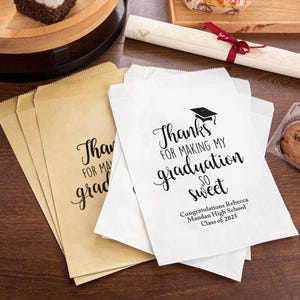 May include: White paper gift bags with black text that reads "Thanks for making my graduation so sweet."  The text is in a cursive font.  The bags also include the text "Congratulations Rebecca Mandan High School Class of 2025".
