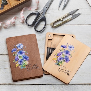 May include: Two wooden boxes with a floral design and the name "Ella" engraved on them. The boxes are open and show a set of needles inside one of the boxes.