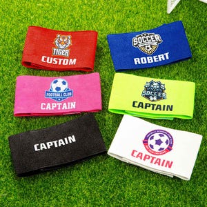 Könnte beinhalten: Sortiment von bunten Fußball-Armbändern mit verschiedenen Designs und Texten. Die Armbänder tragen Texte wie "Kapitän", "Fußball", "Fußballclub", "Tiger", "Benutzerdefiniert" und "Robert".