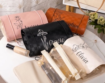 May include: A collection of personalized cosmetic bags in various colors, including pink, black, and orange. Each bag features a floral design and a name. Clear cosmetic pouches with gold zippers are also visible.
