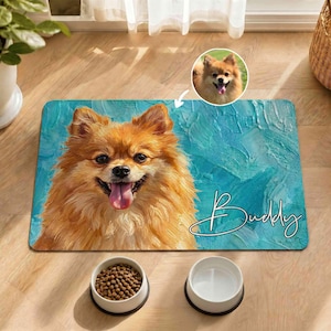 Puede incluir: Una alfombrilla rectangular para mascotas con un retrato pintado de un perro Pomerania naranja esponjoso con la lengua fuera sobre un fondo azul verdoso texturizado. El nombre Buddy está escrito en letra cursiva blanca junto a una foto circular.