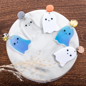 Peut inclure: Cinq paires de boucles d'oreilles fantômes irisées sur une assiette blanche. Les fantômes sont en plastique transparent et de différentes couleurs, notamment blanc, bleu et irisé.