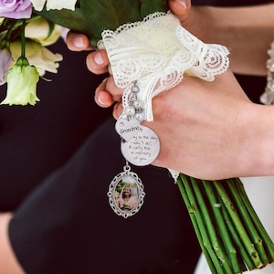 Può includere: Un bouquet da sposa con un involucro di pizzo bianco e un ciondolo d'argento. Il ciondolo presenta una foto e il testo "Nonna, oggi è il giorno in cui dico di sì, porto questo in memoria di te."