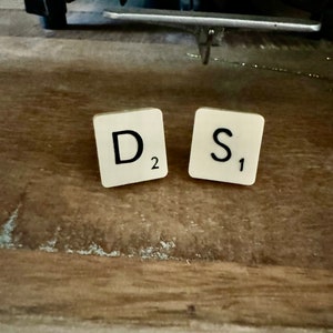 May include: Two white Scrabble tiles with black letters. The first tile has the letter "D" and the number "2". The second tile has the letter "S" and the number "1".