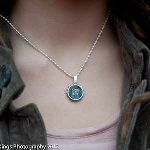 May include: A silver chain necklace with a black and silver pendant that says "SHIFT KEY" in white lettering.
