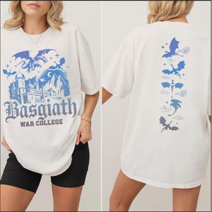 May include: Cream-colored t-shirt featuring a blue and purple graphic of a castle, dragons, and the text "Basgiath War College" on the front. The back of the shirt displays a vertical line of dragon illustrations in blue and purple.