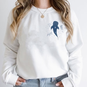 May include: White sweatshirt featuring a navy blue whale shark design with a turtle, jellyfish, and starfish. The graphic is on the upper left chest area. The sweatshirt is a long-sleeved, crew neck style.