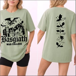 May include: Sage green t-shirt featuring a black graphic of a castle, dragons, and the text "Basgiath War College" on the front. The back of the shirt displays a series of dragon silhouettes. A casual, fantasy-themed garment.
