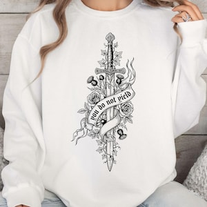 May include: White sweatshirt featuring a black and white illustration of a sword entwined with roses, thistles, and ivy. A banner across the sword reads "you do not yield". The design is centered on the front of the garment.