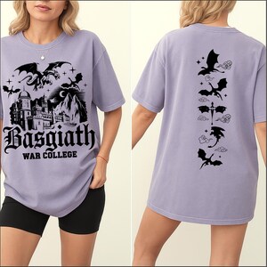 May include: A light purple t-shirt with a black graphic featuring a dragon, castle, and the text "Basgiath War College" on the front. The back of the shirt displays a series of dragon silhouettes.