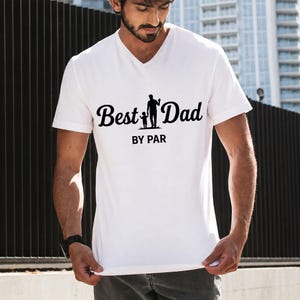 May include: White V-neck t-shirt with the text "Best Dad BY PAR" in black script. The graphic features a silhouette of a father and child. The shirt is made of a soft material.
