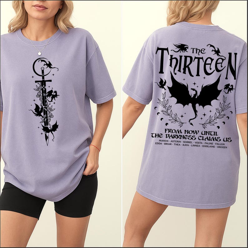 May include: A lilac-colored t-shirt with a black graphic on the front featuring a sword, flowers, and winged creatures. The back of the shirt displays the text "THE THIRTEEN" and "FROM NOW UNTIL THE DARKNESS CLAIMS US."