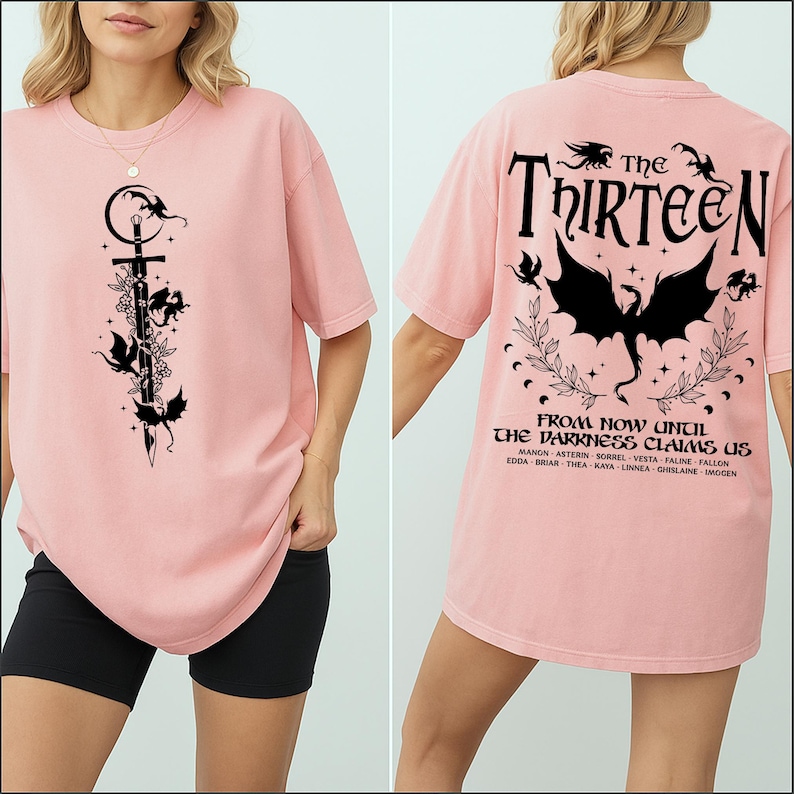 May include: A light pink t-shirt featuring a black graphic of a sword, flowers, and bats. The back of the shirt displays the text "The Thirteen" above a bat graphic and the phrase "From Now Until The Darkness Claims Us."