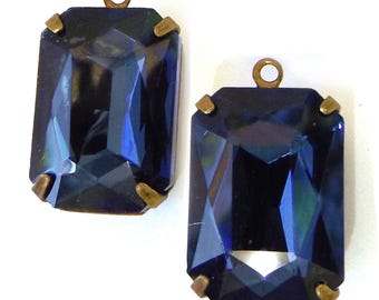 Puede incluir: Dos colgantes rectangulares de cristal azul oscuro con detalles metálicos color latón. Cada colgante tiene un lazo en la parte superior para colgar. Los cristales tienen un diseño facetado, creando un efecto brillante.