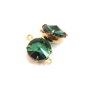 May include: Two emerald green glass connector charms with gold-tone metal settings. The charms have a faceted design and are perfect for adding a touch of sparkle to jewelry projects.