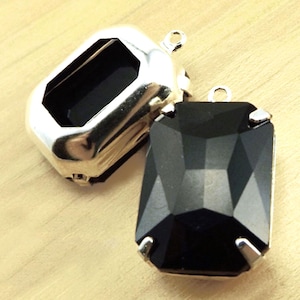 May include: Two silver-toned metal settings for a black crystal pendant. The settings have a loop at the top for attaching to a chain or cord.