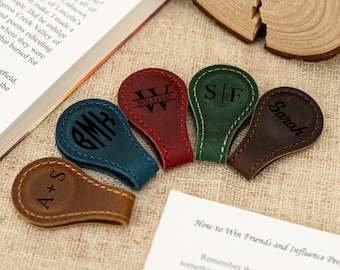 May include: Five leather book markers with different personalized monograms. The markers are in various colors, including brown, blue, red, green, and dark brown. The monograms are in black.