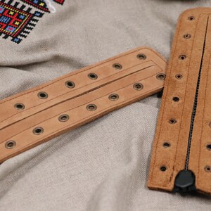May include: Two brown leather bracelets with metal eyelets and a zipper closure.