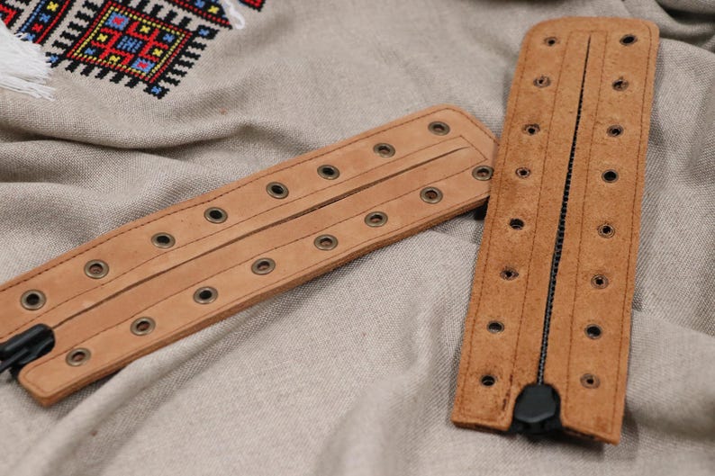 May include: Two brown leather bracelets with metal eyelets and a zipper closure.