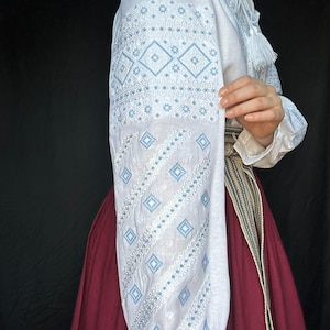 Puede incluir: Blusa blanca bordada con patrones geom&eacute;tricos azules y blancos. La blusa tiene mangas largas y un detalle de borla en el cuello.