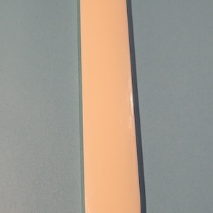 May include: A bone folder, a tool used in crafts like bookbinding and paper crafts, is shown against a light blue background. The folder is made of a smooth, off-white material and has a pointed tip.