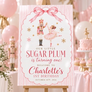 May include: A rectangular birthday sign with a pink and white striped background, featuring a pink bow at the top, a nutcracker, and a ballerina. Text reads: OUR LITTLE SUGAR PLUM is turning one! WELCOME TO Charlotte's 1ST BIRTHDAY OCTOBER 18TH, 2026.