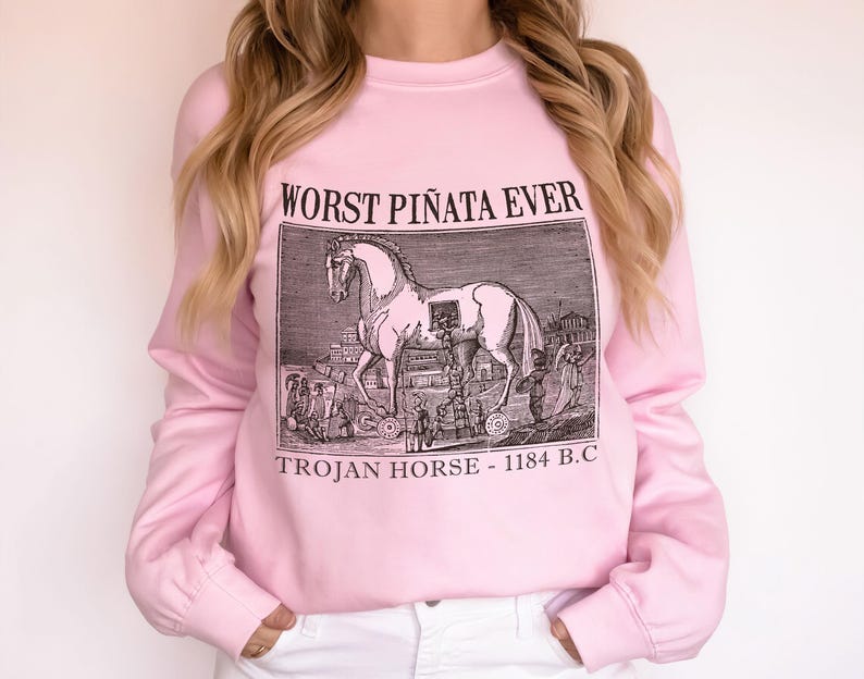 May include: Pink long-sleeve sweatshirt with the text "WORST PI&Ntilde;ATA EVER" above a black and white illustration of the Trojan Horse. The text "TROJAN HORSE - 1184 B.C" is below the illustration.