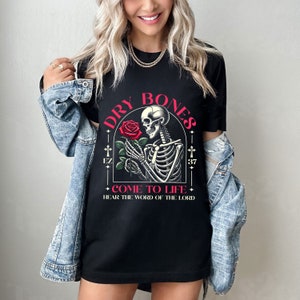 May include: Black t-shirt with a graphic of a skeleton holding a red rose. The text "DRY BONES COME TO LIFE HEAR THE WORD OF THE LORD" is printed on the shirt.