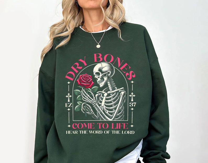 May include: Dark green sweatshirt with a graphic print of a skeleton holding a rose. The text "DRY BONES" is written in pink above the skeleton and "COME TO LIFE" is written below the skeleton. The text "HEAR THE WORD OF THE LORD" is written below the graphic.