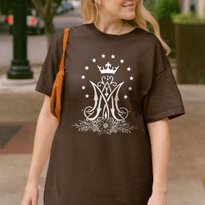 May include: A brown t-shirt featuring a white graphic of a crown, stars, and the letters "M" and "A" intertwined. The graphic is surrounded by a floral design.