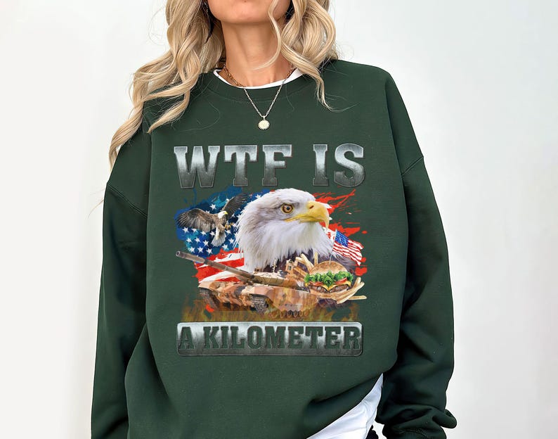 May include: Dark green sweatshirt featuring a graphic of an American bald eagle, the American flag, and the text "WTF IS A KILOMETER". The design includes a tank and a burger. The sweatshirt is a casual style.