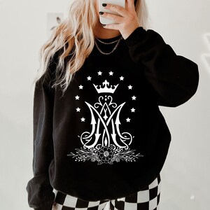 May include: Black sweatshirt featuring a white graphic of a crown, a stylised "M" with a floral design, and a circle of stars.