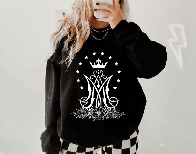 May include: Black sweatshirt featuring a white graphic of a crown, a stylised "M" with a floral design, and a circle of stars.