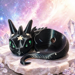May include: A black dragon figurine with star details and green eyes. The dragon is lying down on a stone surface, with a curled tail. The background is a colorful, starry sky. A fantasy-themed item.
