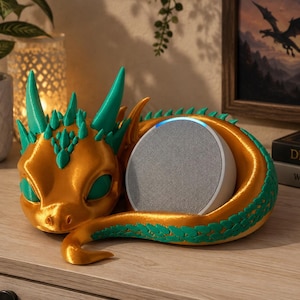 May include: A gold and teal dragon-shaped stand designed to hold a circular smart speaker. The dragon features a metallic gold body with teal spikes along its head and back, curled around a grey fabric-covered smart speaker with a light ring.