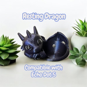 May include: A dark blue dragon-shaped accessory, designed to hold an Echo Dot 5. The dragon is in a resting pose with large eyes and a textured surface. The text "Resting Dragon" and "Compatible with Echo Dot 5" are visible.