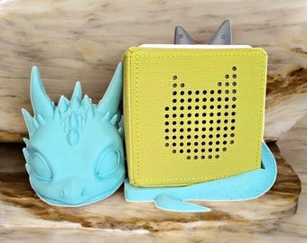 Puede incluir: Una figurita de dragón azul claro sosteniendo un altavoz amarillo con una rejilla de altavoz con forma de gato.